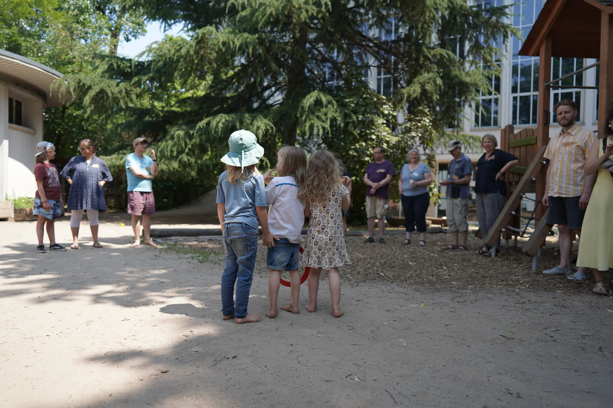 Drei Kinder stehen mit dem Rücken zur Kamera, im Hintergrund einige Erwachsene